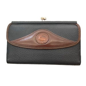 May include: A black pebbled leather wallet featuring a brown leather arched overlay on the front flap. The wallet includes a gold-tone metal kiss-lock closure at the top and a circular brown leather patch embossed with a logo in the center.