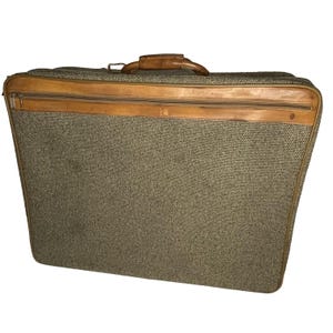 May include: A vintage brown tweed suitcase with a leather handle and trim. The suitcase has a textured fabric exterior and a zipper closure.