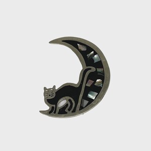 以下が含まれることがあります： 黒猫のシルエットと真珠貝の象嵌が施された銀の三日月形のブローチです。