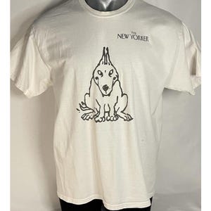 Peut inclure: T-shirt blanc cassé avec une illustration à l'encre noire d'un chien assis. Le chien a une crête distinctive et pointue. Le texte "THE NEW YORKER" est imprimé en noir au-dessus du chien. Le t-shirt a des manches courtes.