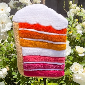 May include: A colorful, layered cake made of felt, with a white frosting top. The cake is a vibrant orange, yellow, pink, and red.