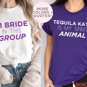 May include: Two white t-shirts with purple text. The first shirt says "#1 Bride in this group". The second shirt is purple and says "Tequila Katie is my spirit animal".