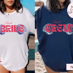 Op de afbeelding: Twee witte T-shirts met een nautisch thema. Het linker shirt zegt "Nauti Bride" met een roze en blauwe schelp-ontwerp. Het rechter shirt zegt "Nauti Crew" met een roze en blauwe schelp-ontwerp. De shirts worden gedragen door modellen.