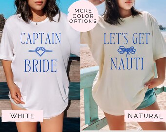 May include: Two women wearing white and cream t-shirts with blue text and nautical rope designs. The white shirt says "Captain Bride" and the cream shirt says "Let's Get Nauti".
