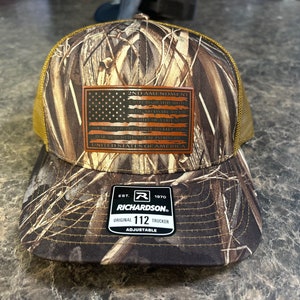 May include: A brown and tan camouflage trucker hat with a brown leather patch that says "2nd Amendment" and has a small American flag on it. The hat has a black mesh back and a black adjustable strap with the words "Richardson" and "Original Trucker" on it.