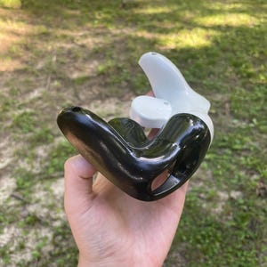 May include: A two-piece object consisting of a glossy black curved component and a smooth white curved component. The black piece features a hollow interior and small circular openings, while the white piece nests partially within the black structure.