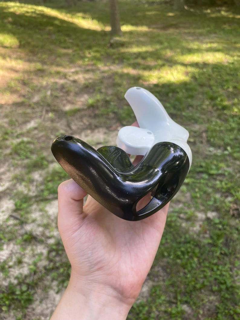 May include: A two-piece object consisting of a glossy black curved component and a smooth white curved component. The black piece features a hollow interior and small circular openings, while the white piece nests partially within the black structure.