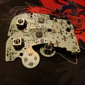 Peut inclure: Gros plan de plusieurs circuits imprimés de manettes de jeu vidéo démontées. Les cartes sont vert clair avec divers composants électroniques, notamment des boutons, des puces et des connecteurs. Les cartes sont disposées sur une surface sombre.