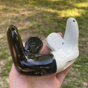 May include: A two-toned video game controller shell featuring a glossy black left side and a glossy white right side. The plastic casing includes molded circular button housing areas, screw holes, and a smooth, ergonomic curved design.