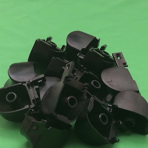 Może przedstawiać: Stos czarnych plastikowych guzików o różnych kształtach i rozmiarach. Niektóre guziki mają podniesiony rant.