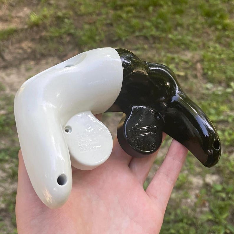 May include: A video game controller shell featuring a split design with a glossy white left side and a glossy black right side. The controller includes a circular button housing on the white section and a circular joystick base on the black side.