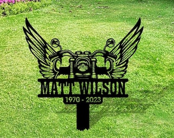 May include: Black metal motorcycle with wings and the text "MATT WILSON 1970 - 2023" on a green grassy lawn.