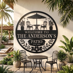 Könnte beinhalten: Ein rundes Wand-Schild aus schwarzem Metall mit einem Scherenschnitt-Design, das ein Terrassenset mit Sonnenschirm, zwei Stühlen und Topfpflanzen zeigt. Der Text lautet WELCOME TO THE ANDERSON'S PATIO EST. 2026, verziert mit Blatt- und Blumenmotiven.