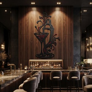 May include: A black wall art piece featuring a stylized cocktail shaker and a martini glass with swirling decorative accents and red details, mounted on a vertical wood panel above a bar counter with various liquor bottles and bar stools.