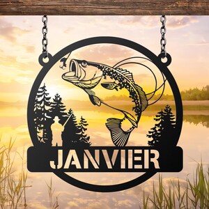 May include: Black metal fishing sign with a leaping fish design, trees, and a fisherman silhouette. The word "JANVIER" is displayed at the bottom. The sign is suspended by chains from a wooden beam, set against a scenic lake backdrop.