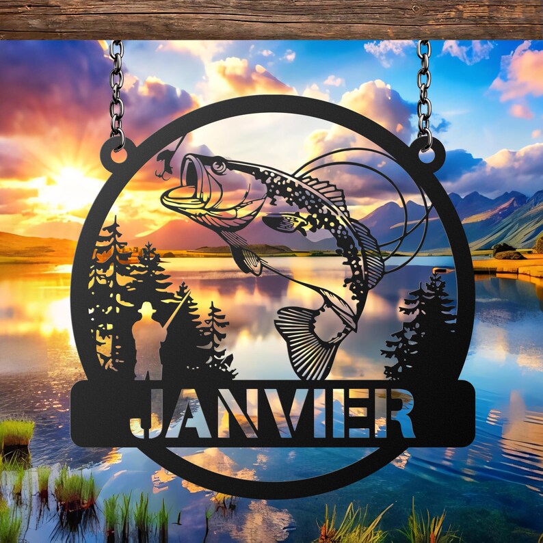 May include: Black metal sign featuring a leaping fish silhouette within a circular frame, suspended by chains. The sign includes a fisherman silhouette, trees, and the word "JANVIER" in a banner, set against a scenic lake and sunset background.