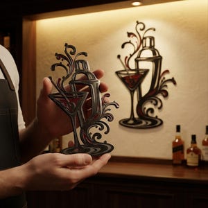 May include: A black metal wall art piece featuring a cocktail shaker and a martini glass with swirling decorative accents. The design includes a red liquid element inside the glass and within the flowing lines of the metalwork, creating a cohesive visual.