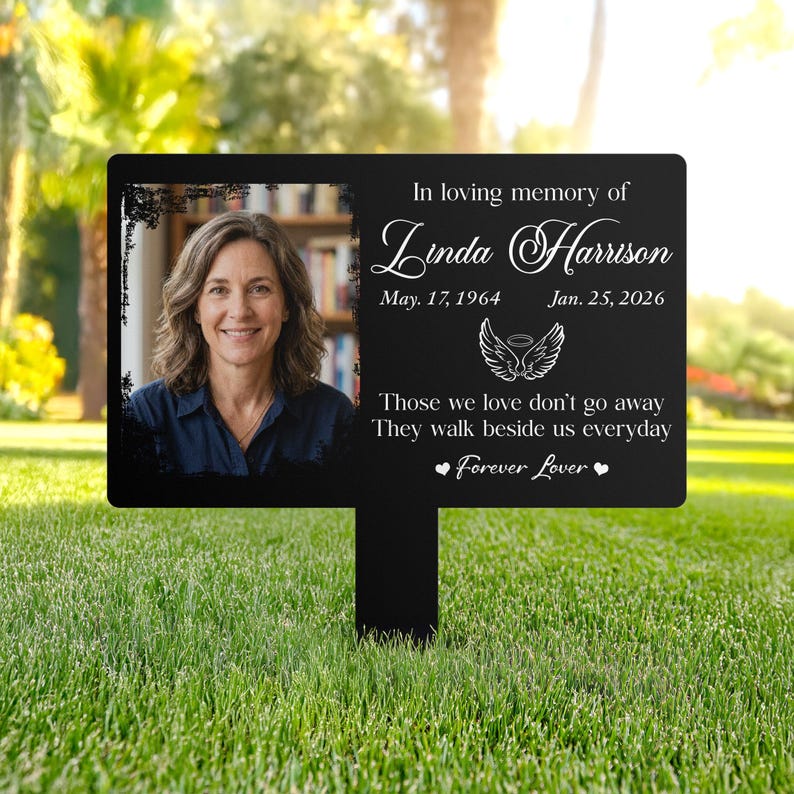 以下が含まれることがあります： 女性の写真と「In loving memory of Linda Harrison」のテキストが入った黒い記念ガーデンステーク。日付、引用句、そして「Forever Lover」という言葉が含まれています。