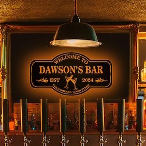 May include: A black and gold sign with the text "Welcome to Dawson's Bar Est. 2024 Cold Drinks, Good Times" hanging on a wall above a bar with taps.