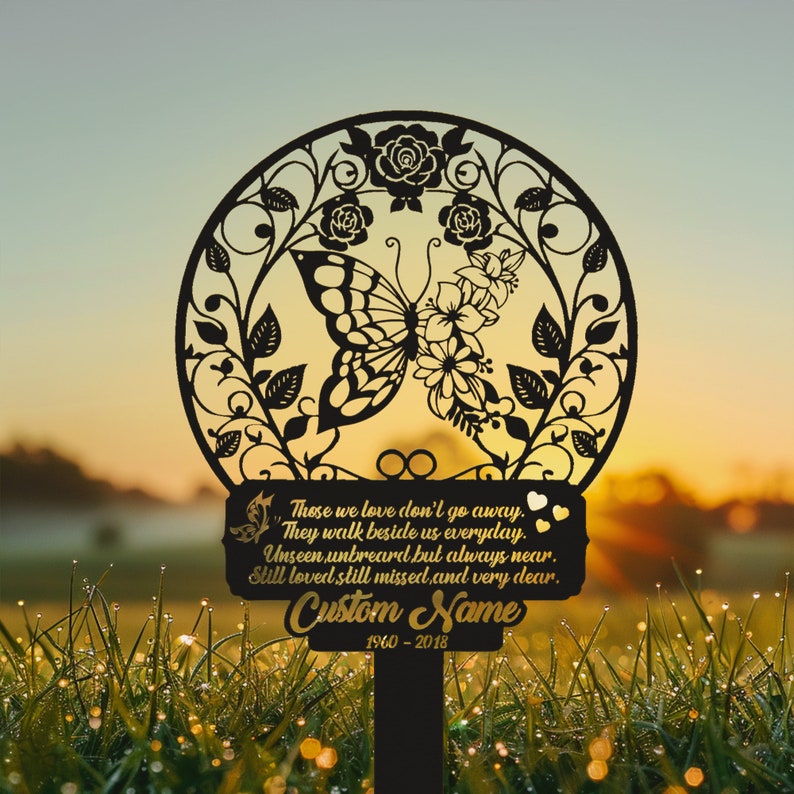 May include: Black metal garden stake with a butterfly design and a sign that reads "Those we love don't go away. They walk beside us everyday. Unseen, unheard, but always near. Still loved, still missed, and very dear. Custom Name 1960-2018"