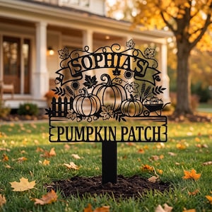 Pode incluir: Uma placa de jardim em metal preto com o texto SOPHIA'S PUMPKIN PATCH. O design inclui recortes de três abóboras, uma pequena cerca, um carrinho de mão cheio de abóboras, talos de trigo, girassóis e várias folhas de outono.