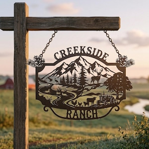 May include: A metal sign for Creekside Ranch, depicting a mountain landscape with a deer, trees, and a tractor. The sign is suspended from a wooden post by chains and has the words "Creekside Ranch" cut out.