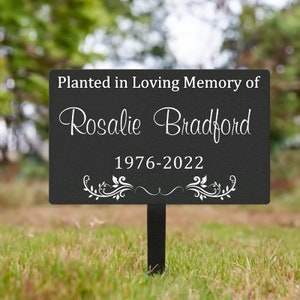 K&ouml;nnte beinhalten: Schwarzes Gedenkschild f&uuml;r den Garten mit wei&szlig;em Text, der lautet: "Gepflanzt in liebevoller Erinnerung an Rosalie Bradford 1976-2022". Das Schild hat unten ein dekoratives Blumenmuster.