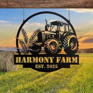 Peut inclure: Panneau métallique noir représentant un tracteur, des épis de blé et le texte "HARMONY FARM EST. 2025". Le panneau est suspendu par des chaînes devant un coucher de soleil sur un champ de foin.