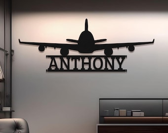 Puede incluir: Arte de pared de avión de metal negro con el nombre "ANTHONY" recortado debajo del avión. La silueta del avión presenta alas, motores y cola. La obra de arte está montada en una pared de color claro.