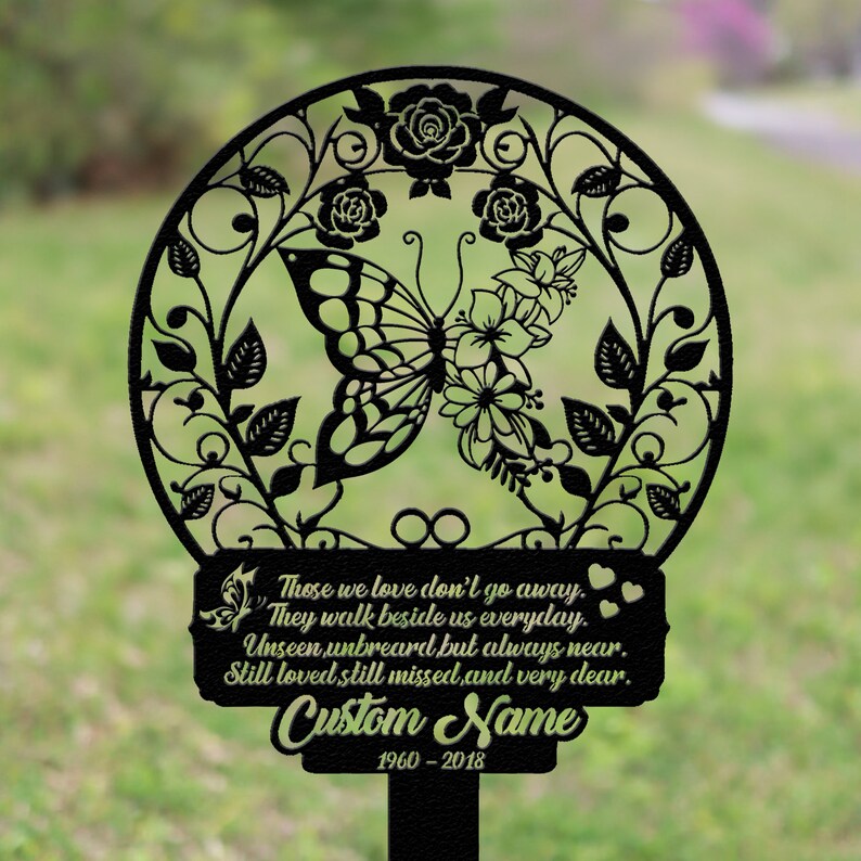 May include: Black metal garden memorial with a butterfly and floral design. The memorial includes the text "Those we love don't go away. They walk beside us everyday. Unseen unheard but always near. Still loved, still missed, and very dear." and a space for a custom name and dates.