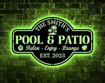 Puede incluir: Letrero de metal negro con las palabras "POOL & PATIO" y "Relax - Enjoy - Lounge" en blanco, con un resplandor de neón verde. El letrero también incluye el apellido "The Smith's" y el año "EST. 2023". El letrero está montado en una pared de ladrillos verdes.