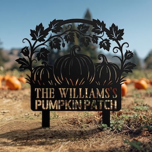 以下が含まれることがあります： 「THE WILLIAMS'S PUMPKIN PATCH」の文字が切り抜かれた黒い金属製の看板。3つのカボチャのシルエットと葉のつるのアーチが特徴です。カボチャ畑に屋外に展示されています。