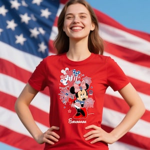 May include: Red t-shirt featuring a Minnie Mouse graphic with patriotic fireworks and bow details. The design incorporates red, white, and blue colors, with the word "Savannah" printed below the character.