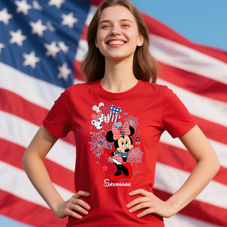 May include: Red t-shirt featuring a Minnie Mouse graphic with patriotic fireworks and bow details. The design incorporates red, white, and blue colors, with the word "Savannah" printed below the character.