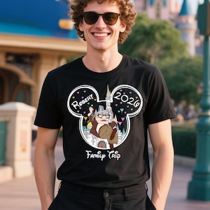 Puede incluir: Camiseta negra con una ilustraci&oacute;n de dibujos animados de un anciano con gafas y un bast&oacute;n, dentro de un contorno de cabeza de Mickey Mouse. El texto "Robert" y "2020" est&aacute;n encima de la ilustraci&oacute;n, con "Family Trip" debajo.