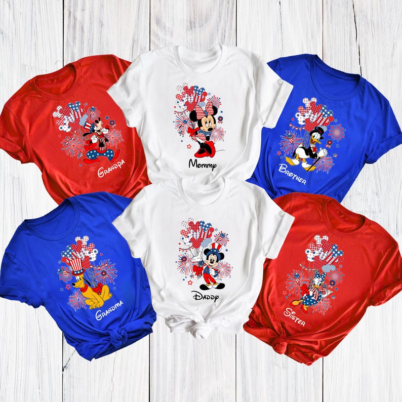 May include: A collection of red, white, and blue t-shirts featuring Disney characters and patriotic fireworks designs. Each shirt has a different character and a family member title, such as "Mommy" and "Grandpa".