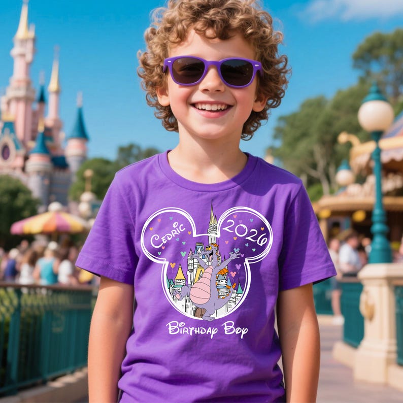 Puede incluir: Una camiseta morada con un dibujo de un drag&oacute;n de dibujos animados, un castillo y el texto "Cedric 2020 Birthday Boy". La camiseta la lleva un ni&ntilde;o con gafas de sol moradas.
