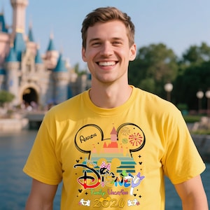Pu&ograve; includere: Una maglietta gialla con un design a tema Disney. Il design include il testo "Aaron", un castello, fuochi d'artificio e le parole "Disney Family Vacation 2020". La maglietta &egrave; indossata da una persona che sorride davanti a un castello.