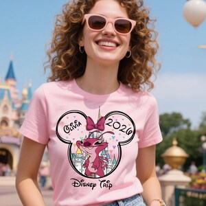 Puede incluir: Camiseta rosa con un personaje de dibujos animados y el texto "Olivia 2026 Disney Trip". El dise&ntilde;o incluye un castillo y un lazo. La persona lleva gafas de sol rosas.
