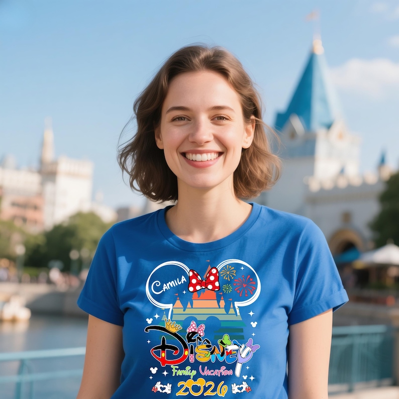 Pu&ograve; includere: Una maglietta blu con un design a tema Disney. Il design include la parola "Disney" in un font colorato, un fiocco di Minnie Mouse e il testo "Family Vacation 2026". La maglietta &egrave; indossata da una persona.