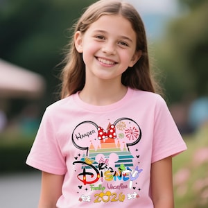 Pu&ograve; includere: T-shirt rosa con grafica a tema Disney. Il design include orecchie di Topolino, un fiocco rosso, fuochi d'artificio e la parola "Disney" in un font colorato. &Egrave; visibile anche il testo "Family Vacation 2020".