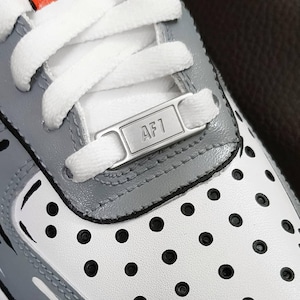 Może przedstawiać: Białe i szare buty sportowe w czarne kropki. Buty mają srebrną metkę z napisem "AF1" z boku.