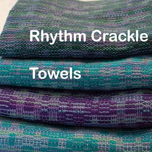 Puede incluir: Una pila de cuatro toallas tejidas en tonos de turquesa, morado y verde. La toalla superior tiene el texto "Rhythm Crackle" impreso en ella. La segunda toalla tiene el texto "Towels" impreso en ella.