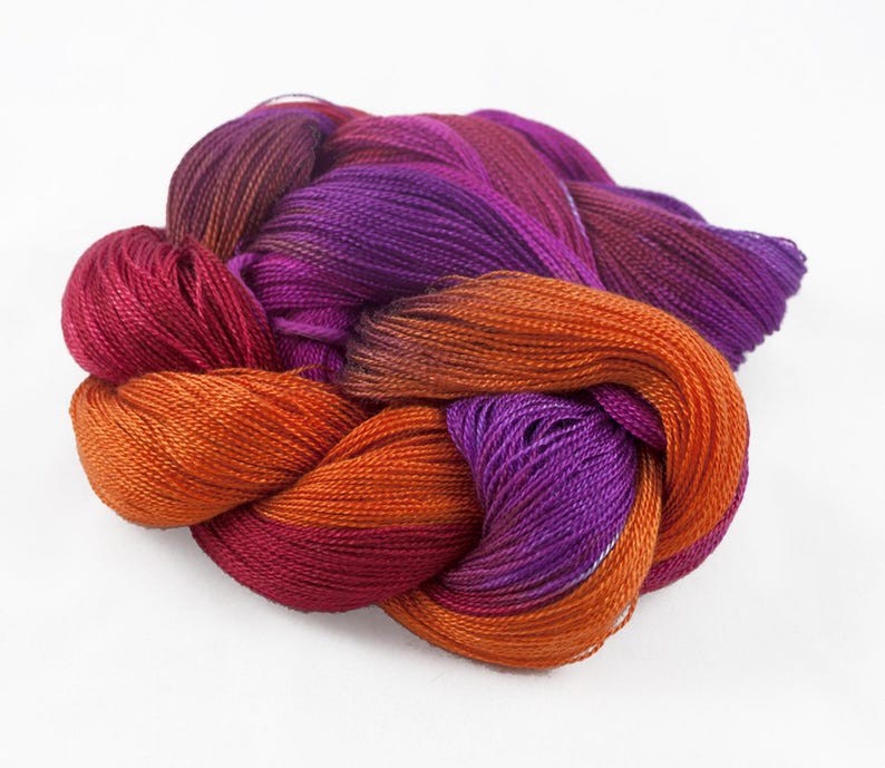 Puede incluir: Un ovillo de hilo colorido en tonos naranja, morado y rojo. El hilo est&aacute; bien enrollado y parece suave, con un ligero brillo. Los colores se mezclan, creando un efecto degradado. Ideal para proyectos de tejido o ganchillo.