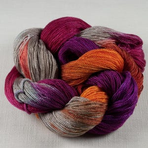 May include: A skein of colorful yarn in shades of fuchsia, orange, purple, and gray. The yarn is tightly wound, with a braided appearance. The yarn is likely used for knitting or crocheting projects.