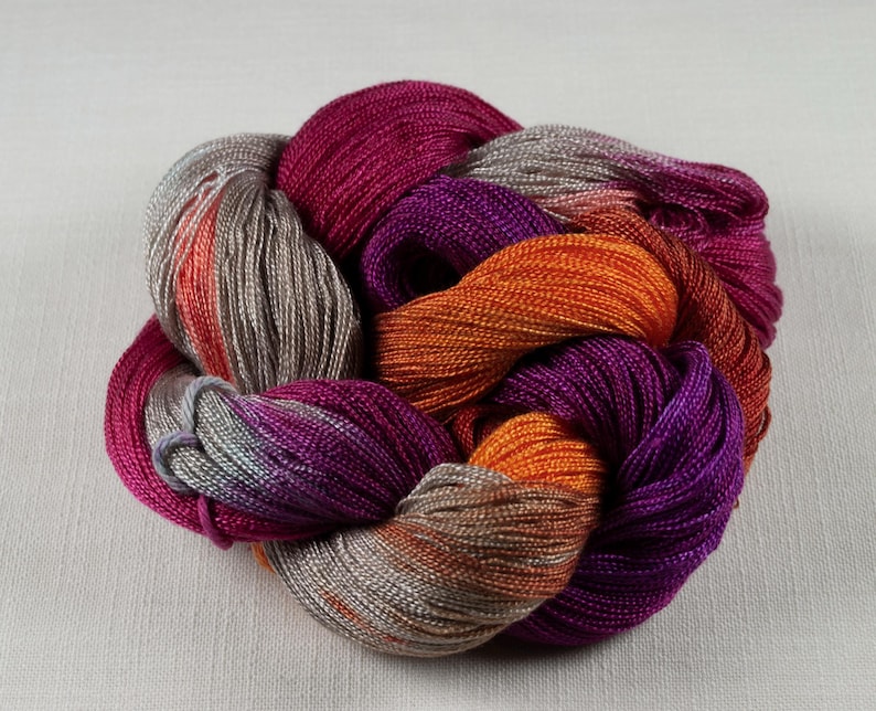 May include: A skein of colorful yarn in shades of fuchsia, orange, purple, and gray. The yarn is tightly wound, with a braided appearance. The yarn is likely used for knitting or crocheting projects.