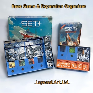 May include: A blue and orange board game organizer with the text "SETI" on the box. The organizer includes compartments for game pieces and cards, with space-themed illustrations. The text "Base Game & Expansion Organizer" is also visible.