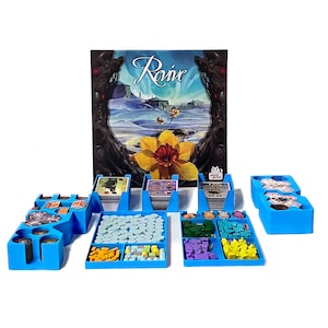 May include: Blue plastic organiser inserts for the board game "Raive". The inserts include compartments for cards, tokens, and tiles. The game box lid is in the background.
