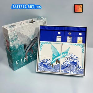 Könnte beinhalten: Ein Brettspiel mit einem Design eines fliegenden Fisches. Die Box ist weiß und türkis mit dem Wort "FINSPAN". Die Spielkomponenten sind weiß mit blauen Wellen- und Fischillustrationen. Der Text "LAYERED.ART.LTD." ist auf der Box.