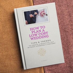 May include: A white book with a pink title "How to Plan a Low Cost Wedding" and a photo of a bride and groom on the cover. The book also includes the text "Tips & Trends to create a beautiful day without spending a fortune!" and a gold clover design.